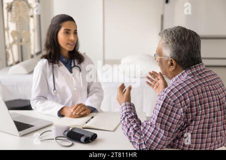 Ernste junge Lateinarztpraxis trifft sich mit einem älteren indischen Patienten Stockfoto