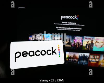 Person, die ein Smartphone mit dem Logo des US-amerikanischen Videostreaming-Unternehmens Peacock TV LLC vor der Website hält. Schwerpunkt auf dem Display des Telefons. Stockfoto