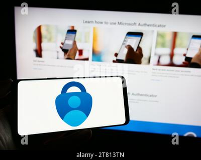 Person, die ein Mobiltelefon mit dem Logo der Authentifizierungs-App Microsoft Authenticator vor der Unternehmenswebseite hält. Schwerpunkt auf dem Display des Telefons. Stockfoto