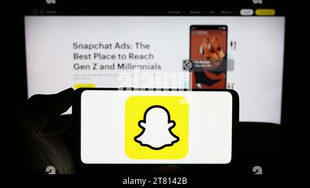 Person, die ein Mobiltelefon mit dem Logo der amerikanischen Multimedia Instant Messaging App Snapchat vor der Business Webseite hält. Schwerpunkt auf dem Display des Telefons. Stockfoto