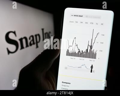 Person mit Smartphone und Webseite des US-amerikanischen Social-Media-Unternehmens Snap Inc. Vor dem Firmenlogo. Konzentrieren Sie sich auf die Mitte des Telefondisplays. Stockfoto