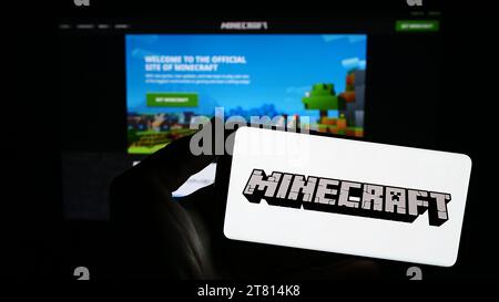 Person mit Smartphone und Logo des Sandbox-Videospiels Minecraft vor der Website. Schwerpunkt auf dem Display des Telefons. Stockfoto