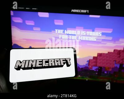 Person, die ein Mobiltelefon mit dem Logo des Sandbox-Videospiels Minecraft vor der Webseite hält. Schwerpunkt auf dem Display des Telefons. Stockfoto