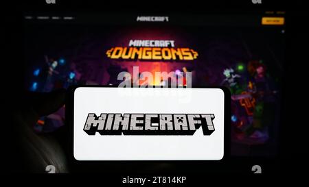 Person mit Handy mit Logo des Sandbox-Videospiels Minecraft vor der Webseite. Schwerpunkt auf dem Display des Telefons. Stockfoto