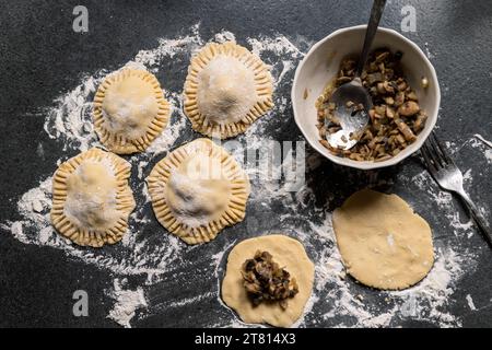 Herstellung glutenfreier Teigtaschen mit Pilzen und Zwiebeln. Dunkelgraue Arbeitsplatte mit Mehl bestreut. Hausgemacht. Stockfoto