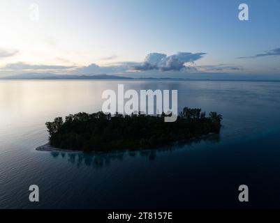Eine idyllische tropische Insel, umgeben von ruhigem Meer, liegt bei Sonnenaufgang in Raja Ampat. Diese abgelegene Region unterstützt eine hohe biologische Vielfalt der Meere. Stockfoto