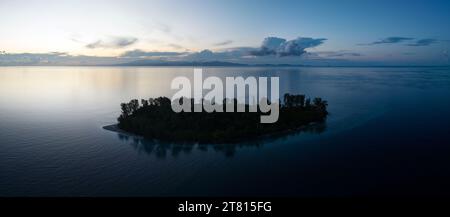 Eine idyllische tropische Insel, umgeben von ruhigem Meer, liegt bei Sonnenaufgang in Raja Ampat. Diese abgelegene Region unterstützt eine hohe biologische Vielfalt der Meere. Stockfoto