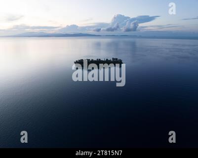 Eine idyllische tropische Insel, umgeben von ruhigem Meer, liegt bei Sonnenaufgang in Raja Ampat. Diese abgelegene Region unterstützt eine hohe biologische Vielfalt der Meere. Stockfoto