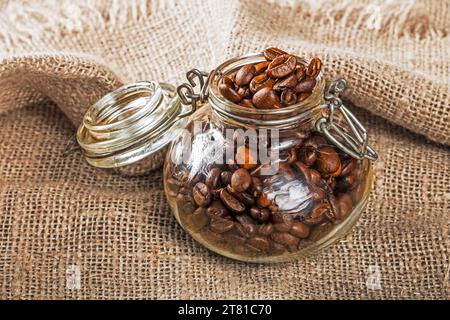 Kaffeemusik. Glasbehälter gefüllt mit Kaffeebohnen auf einer Serviette mit Sackleinen. Stockfoto