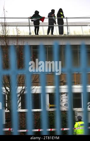 Southampton, Hampshire, Großbritannien. November 2023. Aktivist hält palästinensische Fahnen, während ein Polizist in einem abgesperrten Gebiet am Boden versucht, sie niederzureden. Palästina-Aktion besetzt das Dach der italienischen Rüstungsindustrie, der Riese Leonardo in seiner Fabrik in Southampton. Leonardo beliefert Israel mit Kampfjets und Waffen, die derzeit im Gazastreifen eingesetzt werden. Palestine Action verlangt, dass Waffenunternehmen, die Waffen für Israel bereitstellen, dauerhaft geschlossen werden. Sie haben angekündigt, dass Unternehmen, die Waffen an die israelischen Streitkräfte verkaufen, und ihre Partnerunternehmen dies tun werden Stockfoto