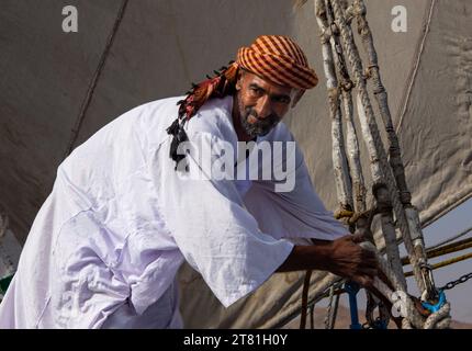 In traditioneller Kleidung bemannt ein Nilbootmann eine Felucca, das traditionelle Boot, das noch immer auf dem Nil zu finden ist Stockfoto