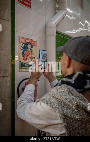 Nahaufnahme eines Mannes, der mit einem Handy eine alte Prinzipis-Illustration fotografiert, die an der gekachelten Wand des zentralen Marktes in Castellon befestigt ist. Stockfoto