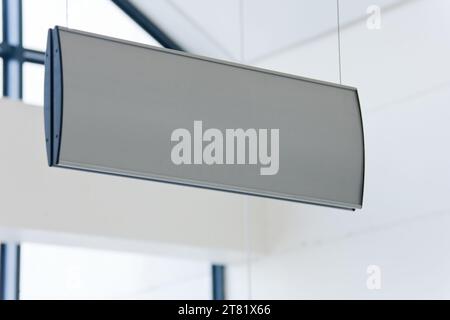 ein leeres weißes mockup-Schild hängt drinnen hoch von der Decke, Fenster im Hintergrund, Tageslicht, Designelemente Stockfoto
