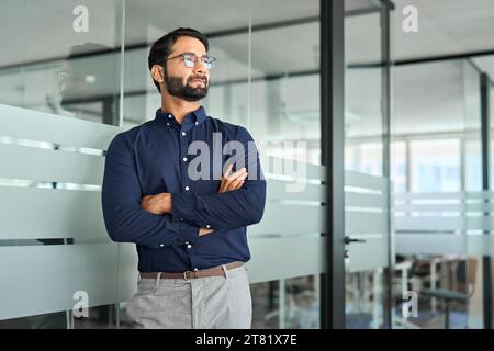 Ernsthafter indischer Geschäftsmann, der wegschaut, im Amt gekreuzte Arme. Stockfoto