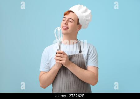 Männliche Konditorin in Schürze mit Schneebesen mit Schlagsamkeit auf blauem Hintergrund Stockfoto
