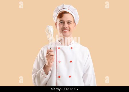 Männliche Konditorin in Uniform mit Schneebesen mit geschlagenem Meringue auf beigefarbenem Hintergrund Stockfoto