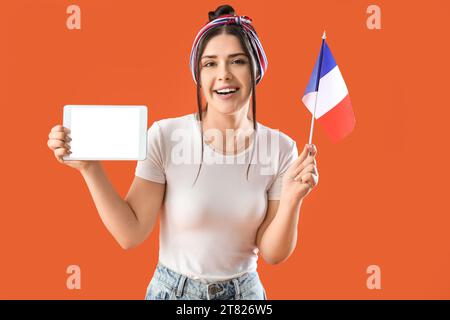 Junge Frau mit Flagge von Frankreich und Tablet-Computer auf orangem Hintergrund Stockfoto