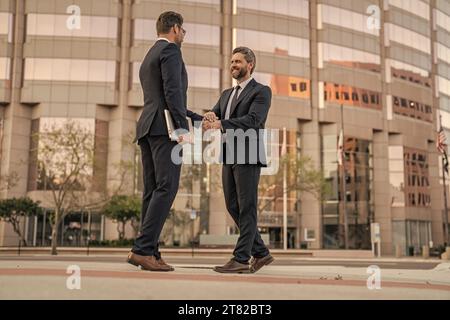 Fröhliche zwei Geschäftsleute, die sich die Hand schütteln. Zwei Geschäftsleute, die draußen die Hand schütteln. Stockfoto