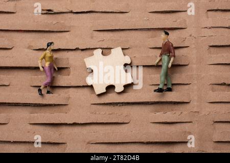 Puzzleteil und winzige Figur des Miniaturmodells von Mann und Frau im Blick Stockfoto