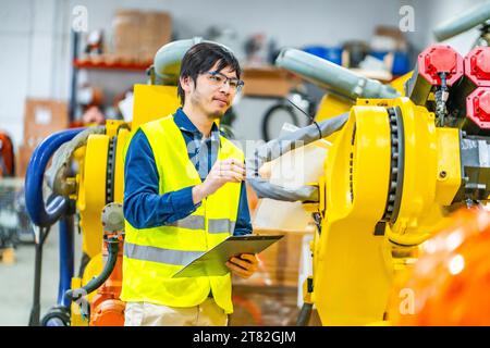 Japanischer junger Ingenieur, der die Produktionslinie von Roboterarmen kontrolliert Stockfoto