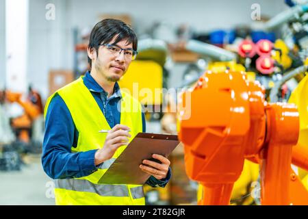 Junger japanischer Ingenieur im Dienst, der eine industrielle Produktionslinie von Roboterwaffen kontrolliert Stockfoto