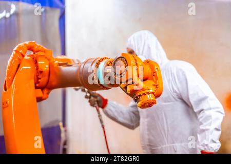 Industrielacker mit Schutzausrüstung lackiert einen Roboterarm mit Sprühnebel in einer industriellen Roboterindustrie Stockfoto