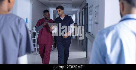 Verschiedene männliche Ärzte mit Tablettengehen im Krankenhauskorridor Stockfoto