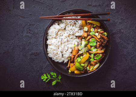 Mit Pilzen, Gemüse und Reis auf dunklem Hintergrund unter Rühren anbraten. Asiatische Küche Stockfoto