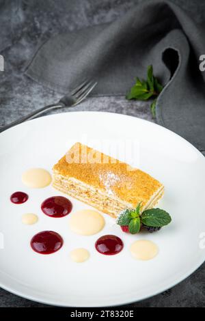 Weißer Biskuitkuchen mit Tropfen Sirup, Minze und Waldbeeren auf einer runden Tellerseite Stockfoto
