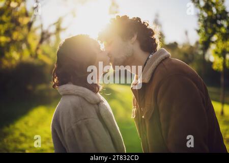 Glückliches, liebevolles Paar, das sich bei Sonnenuntergang im Park küsst. Stockfoto