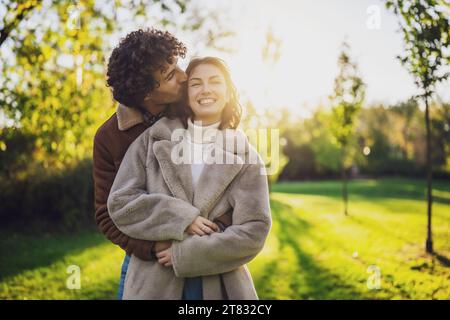 Glückliches, liebevolles Paar, das sich bei Sonnenuntergang im Park umschließt und küsst. Stockfoto