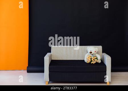 Sofa mit einem Bären mit Blumen auf schwarzem Hintergrund im Zimmer Stockfoto