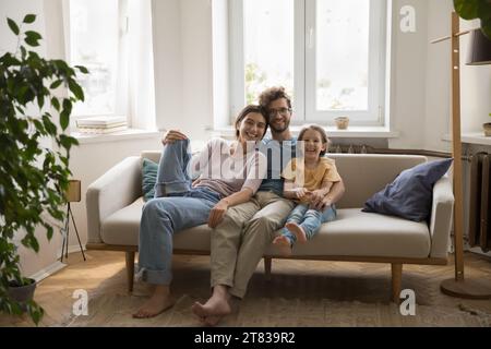 Porträt einer liebevollen Familie, die auf einem Sofa sitzt und eine Kamera aussieht Stockfoto