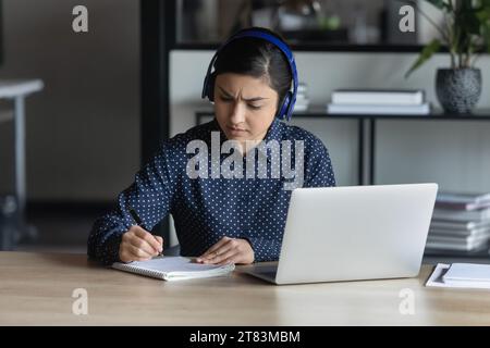 Konzentrierter indischer Student in Kopfhörer, der Webinar auf Laptop ansieht Stockfoto
