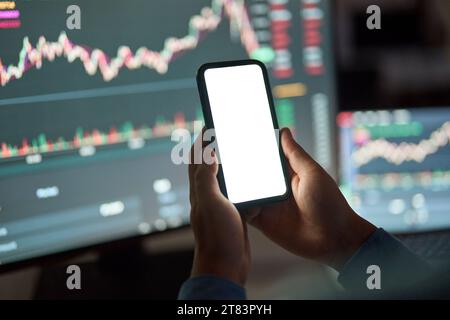 Händler, der das Handy hält, weiß-Mock-up-Bildschirm auf dem Hintergrund des Börsenhandels. Stockfoto