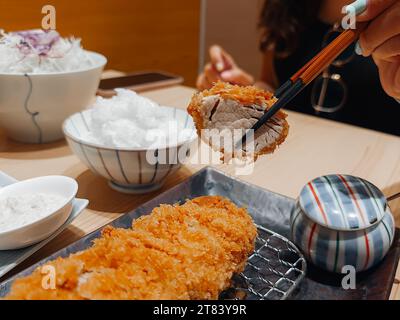 Verwenden Sie hölzerne Essstäbchen, um frittiertes Schweinefleisch oder Tonkatsu in einem japanischen Restaurant zu zangen Stockfoto