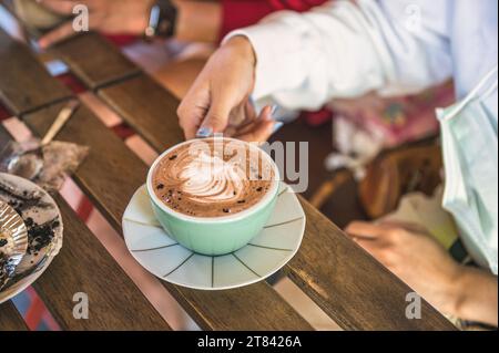 Frau Hand hält eine Tasse heiße Schokolade mit Muster aus frischer Milch im Café Stockfoto
