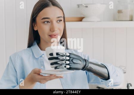 Eine junge Frau mit einer bionischen Hand hält bewundernswert einen Becher, eine Verschmelzung von Menschlichkeit und fortschrittlicher Robotik Stockfoto