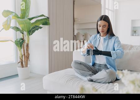 Eine ruhige Frau mit bionischem Arm sitzt bequem zu Hause und zeigt die Harmonie zwischen Technologie und Alltag Stockfoto
