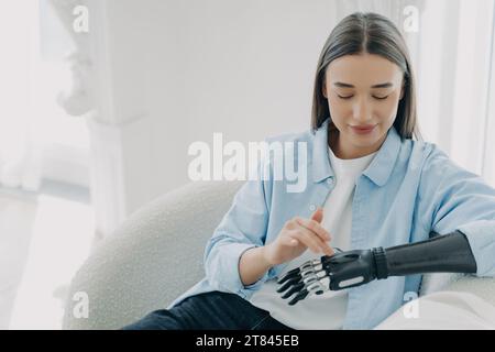 Zufriedene Frau mit bionischer Hand, die sanft ihren Unterarm berührt und die Mischung aus Menschlichkeit und Technologie zeigt Stockfoto