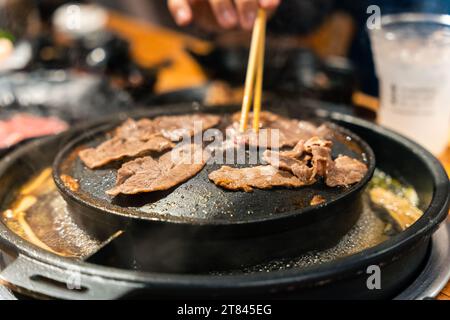 Geben Sie Schweine und Rindfleisch mit einem Essstäbchen auf einem Holzkohleofen mit Suppe im BBQ-Restaurant Stockfoto