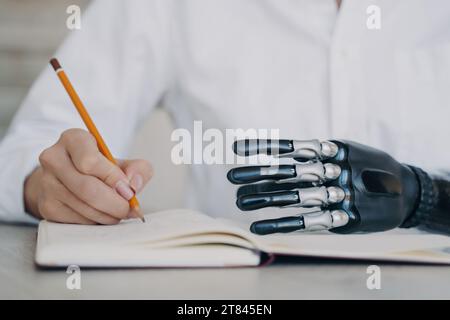 Fokussiertes individuelles Schreiben in Notizbüchern mit mechanischer Handprothese und adaptiver Technologie Stockfoto