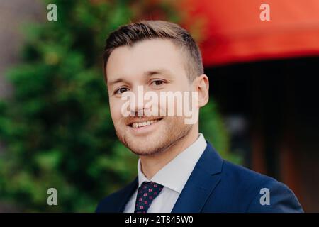 Selbstbewusster Geschäftsmann in blauem Anzug mit einem einladenden Lächeln im Freien Stockfoto