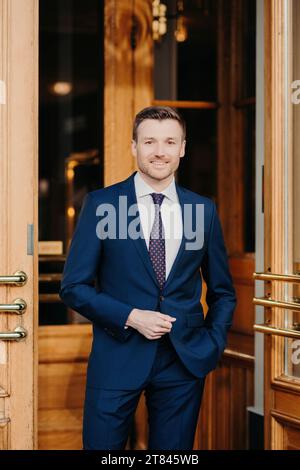 Elegant gekleideter Mann in einem maßgeschneiderten blauen Anzug und Krawatte, der selbstbewusst vor einem Luxushotel steht Stockfoto
