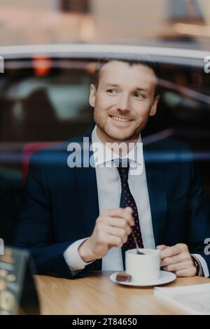 Ruhiger Geschäftsmann, der Kaffee hinter dem Fenster genießt, städtische Reflexionen, ruhige Momente Stockfoto