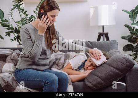 Trauriges krankes Kind Mädchen, das auf der Couch zu Hause liegt, fühlen Fieber, sich Erkältungsgrippe Grippe zu fangen. Ängstliche junge kaukasische Mutter, die Telefon an Ohr hält, macht einen Anruf zu tun Stockfoto