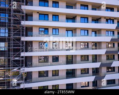 Drohnenflug entlang der Fassade eines modernen Wohngebäudes, das von Gerüsten umgeben ist. Stockfoto