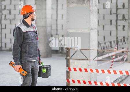 Ein Vorarbeiter inspiziert eine neue Wohnung, bevor er mit der Arbeit beginnt. Bauherr in einheitlichem Werkzeugkasten und Nivellierwerkzeug auf der Baustelle, Kopierraum Stockfoto