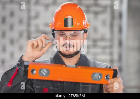 Bauarbeiter Porträt mit Nivellierwerkzeug, kaukasischer bärtiger Mann mit Schutzhelm, Schutzbrille und Uniform, Bauen und Inspektion Stockfoto