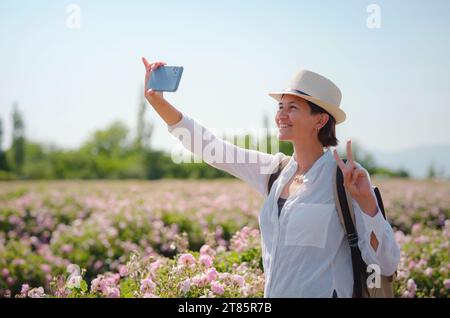 Frau genießt das Aroma und macht Fotos in ihrem Smartphone auf dem Feld von Damaszenerrosen an sonnigen Sommertagen. Village Guneykent in der Region Isparta, Türkei, ein wahres Paradies für Ökotourismus. Stockfoto